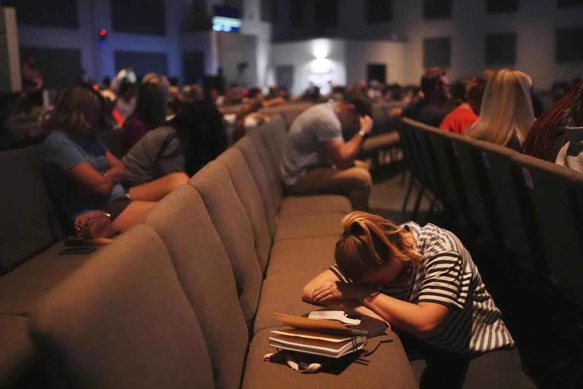 A woman rests her head on a church seat.
